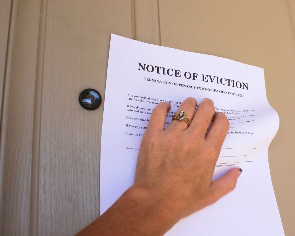 Woman's hand grabbing a letter stating Eviction Notice off a house door.