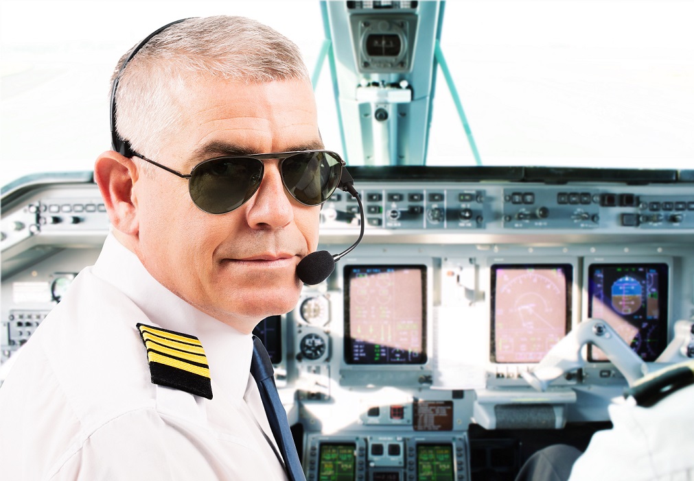Airline pilot wearing uniform with epaulettes and headset working in airliner during flight.