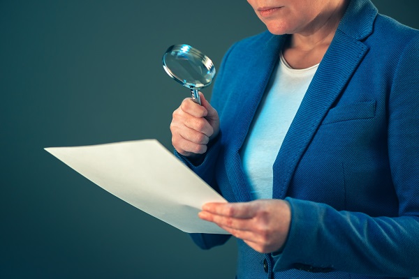 Female tax inspector looking at corporate financial documents with magnifying glass