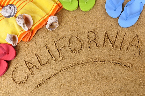 Beach background with towel and flip flops and the word California written in sand.